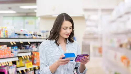 Una mujer comparando Allegra® con otro medicamento en el pasillo de alergias de la farmacia